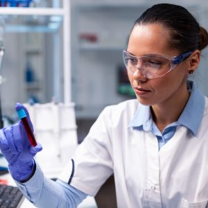 Specialist chemist looking at medical vacutainer with blood analyzing microbiology clinical expertise. Researcher woman doctor discovering illness infection working in hospital laboratory